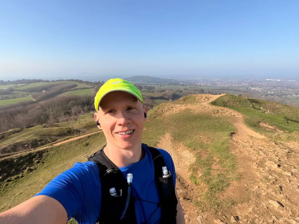Graham out running on the hills, in a yellow cap and blue running top