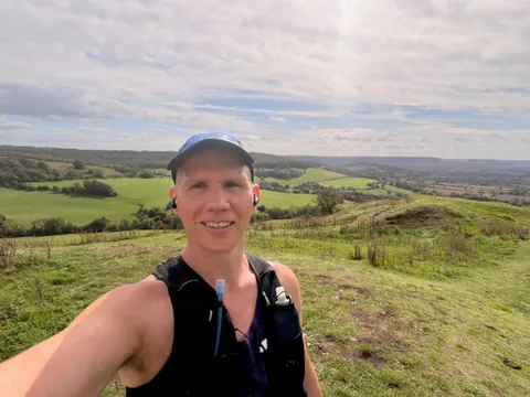 Graham on a grassy hillside in a blue cap and running vest