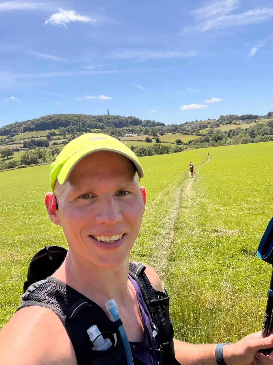 Graham smiling on a sunny green hillside with a trail winding behind him
